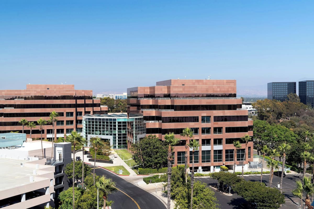 A modern building complex with multiple floors, surrounded by palm trees and a clear sky.