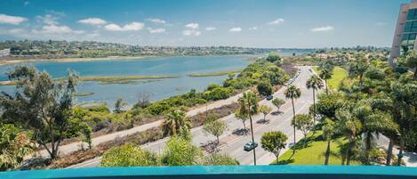 A balcony with a view of a lake, a road, and a building in the distance.