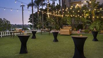 An outdoor seating area with round tables and chairs, string lights, and a view of a building and palm trees.