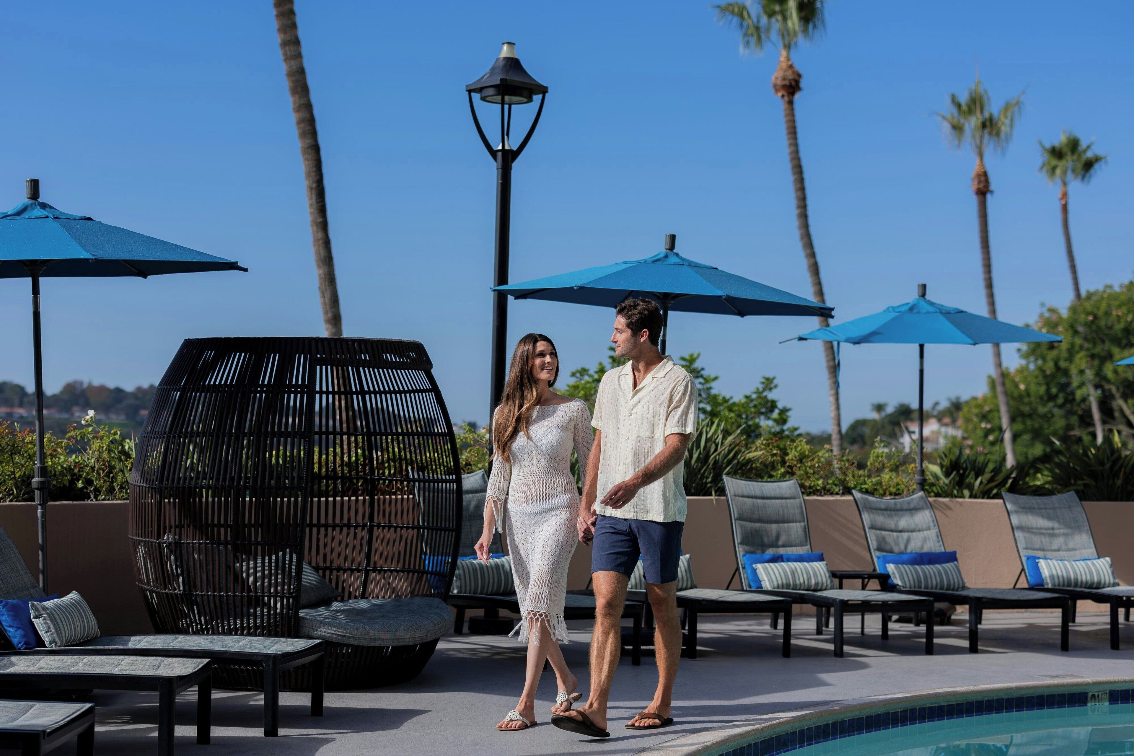 A couple walking by a poolside lounge area with umbrellas and lounge chairs.