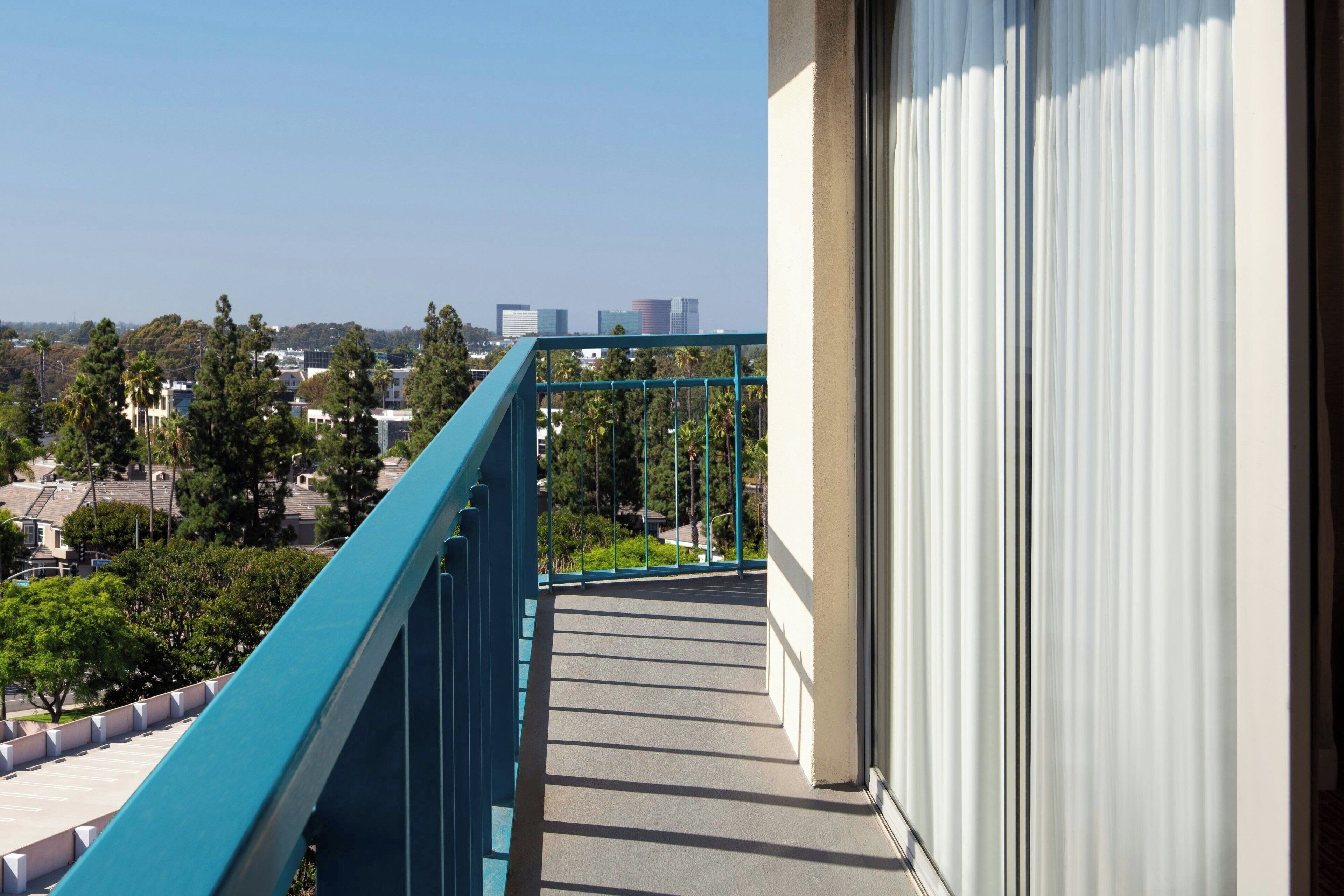 A balcony with a view of a cityscape, including buildings and trees.