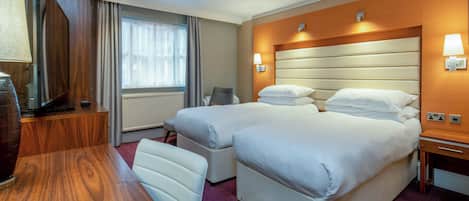 A hotel room with two beds, a desk, a chair, a lamp, and a window with curtains.