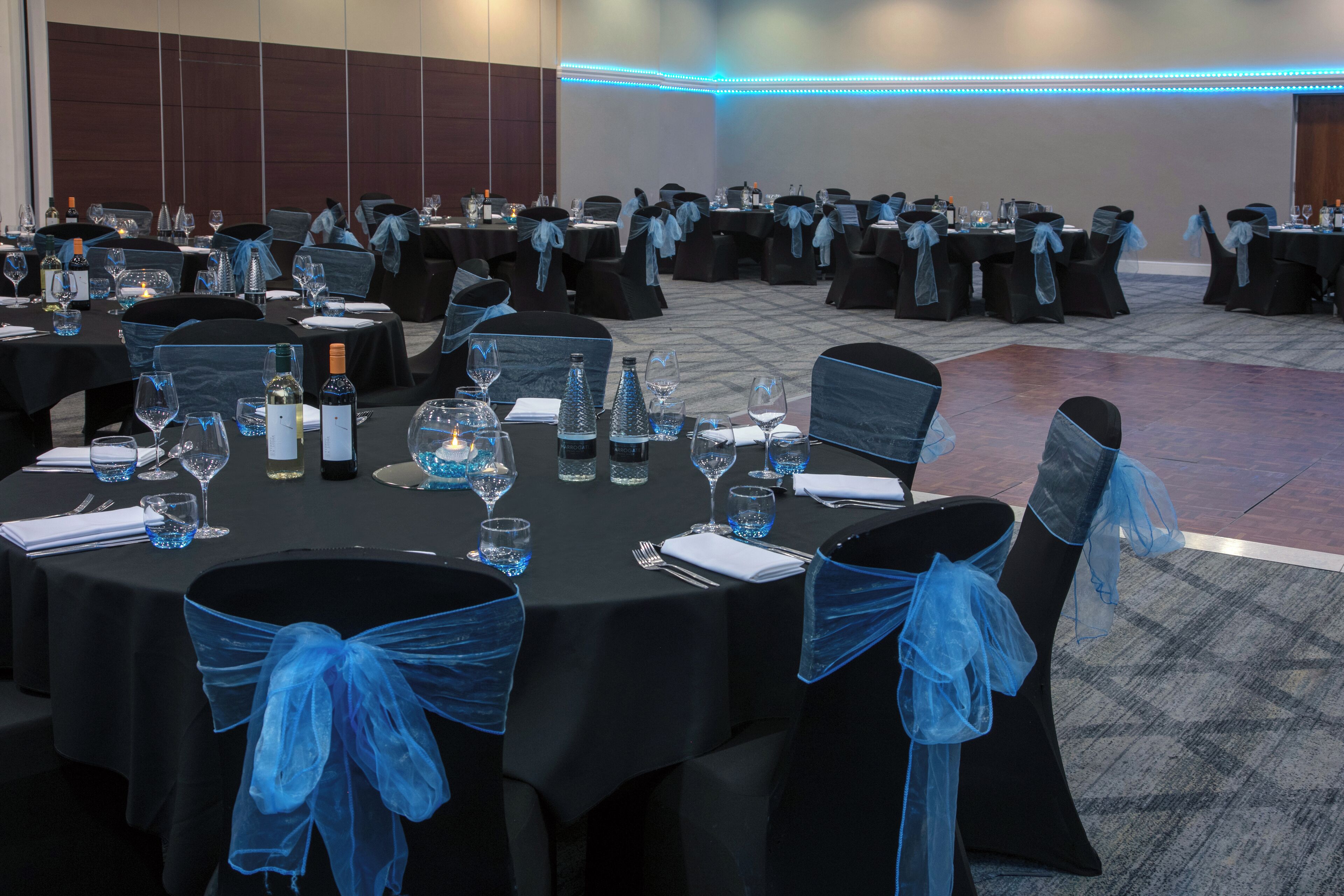 Une salle de banquet avec des tables rondes dressées pour le repas, chaque table étant agrémentée de chaises ornées de rubans bleus.
