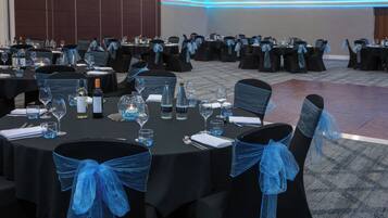 A banquet hall with round tables set for dining, each with chairs adorned with blue sashes.