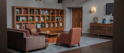 A modern living room with a sofa, armchair, and a wooden bookshelf filled with decorative items.