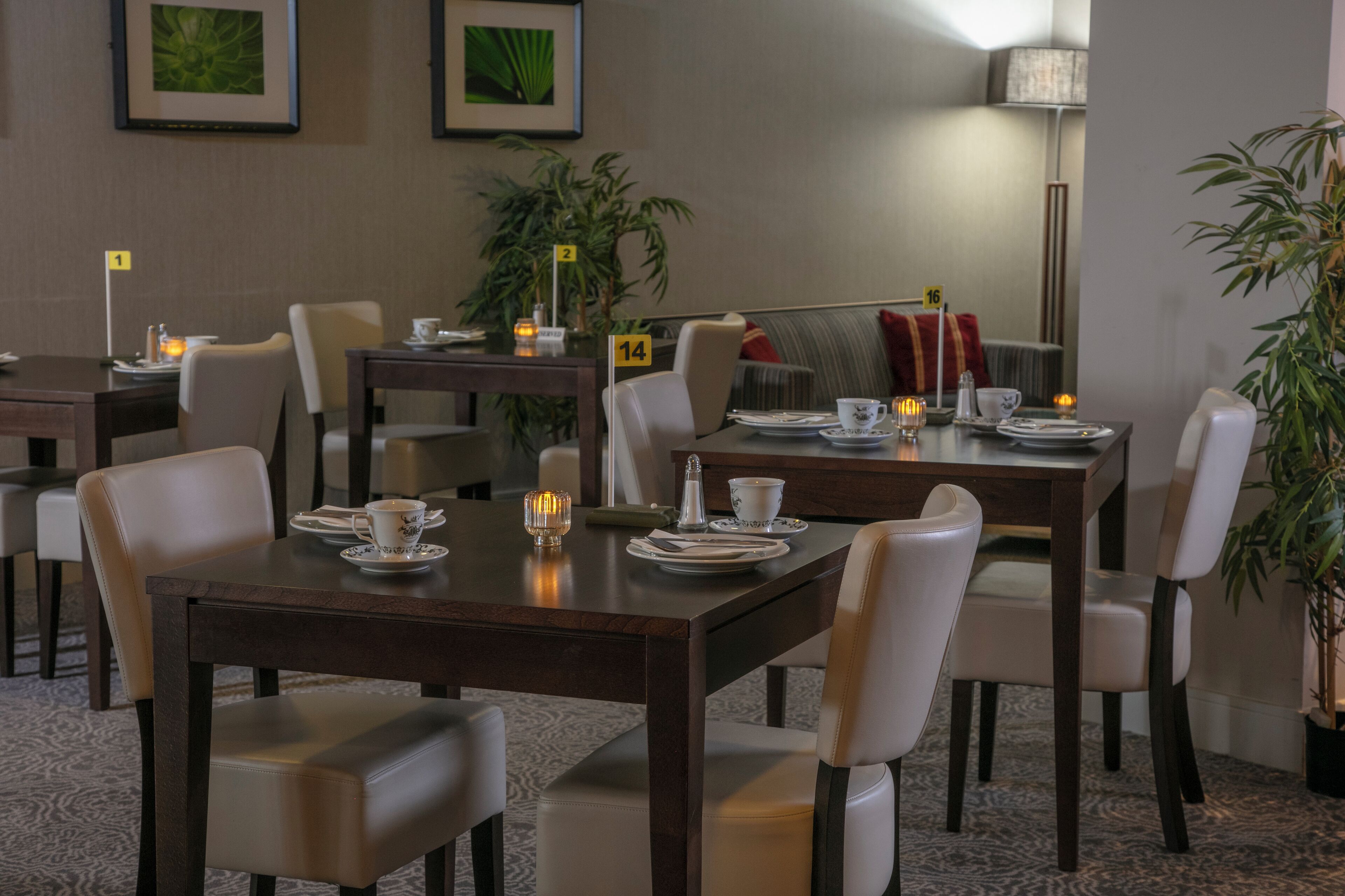 A dining area with tables set for four, chairs, and a lamp.