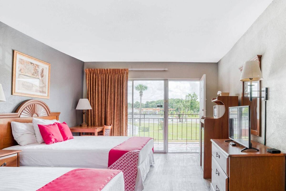 A hotel room with two beds, a desk, a TV, and a balcony with a view.