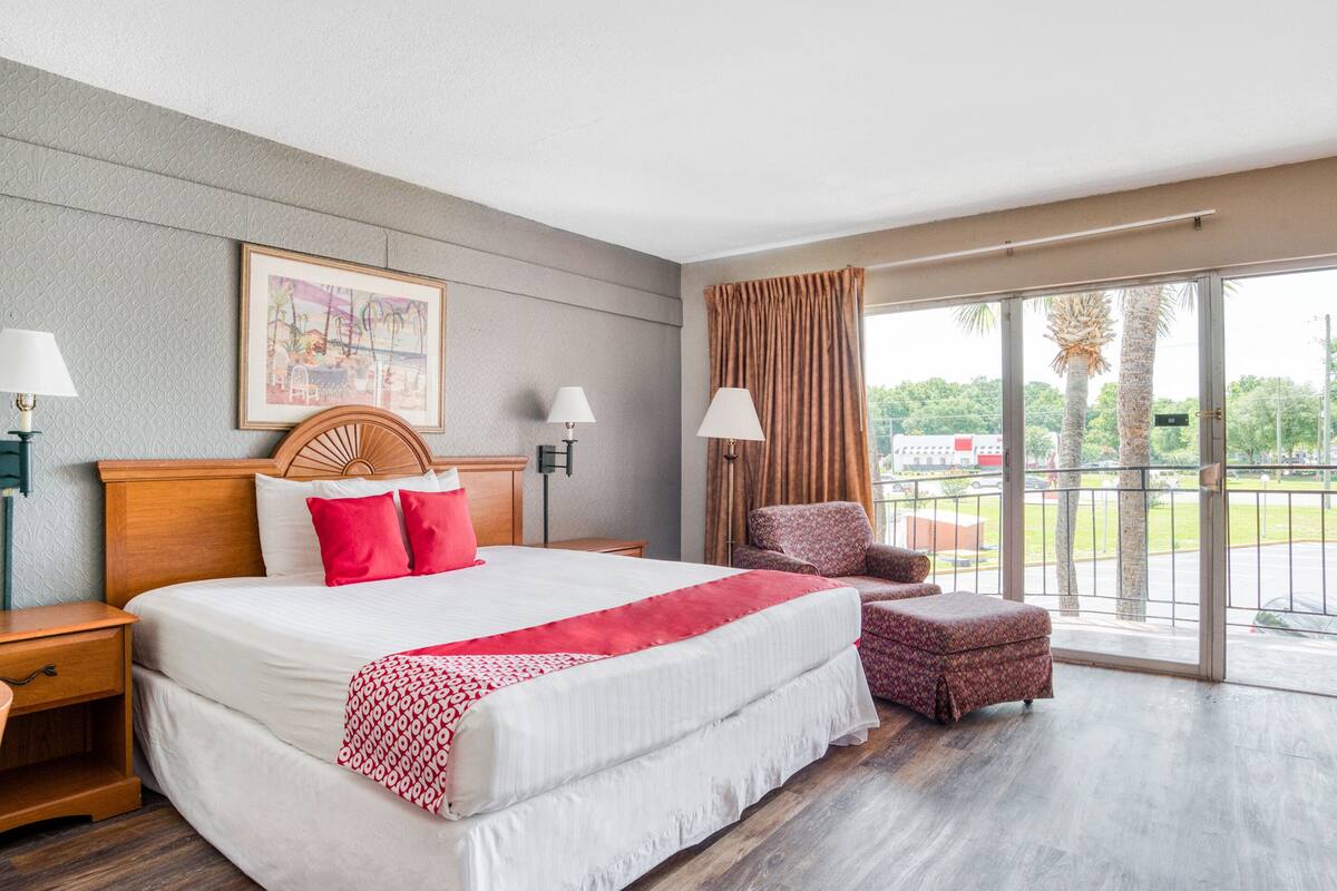 A hotel room with a large bed, two bedside tables, a chair, a window with curtains, and a view of the outdoors.