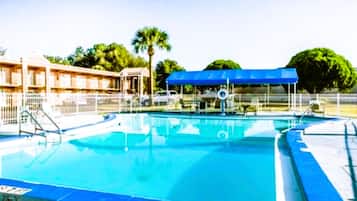 Relax by the pool surrounded by lush trees and a nearby building.