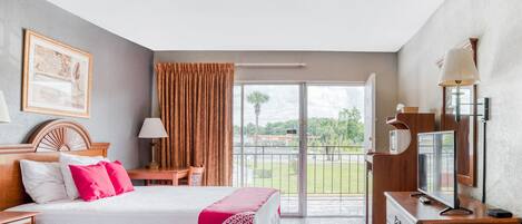 Een hotelkamer met twee bedden, een bureau, een televisie en een balkon met uitzicht op groen.