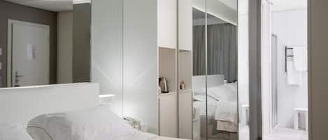 A modern hotel room with a large bed, a walk-in closet, and a bathroom visible through a glass door.