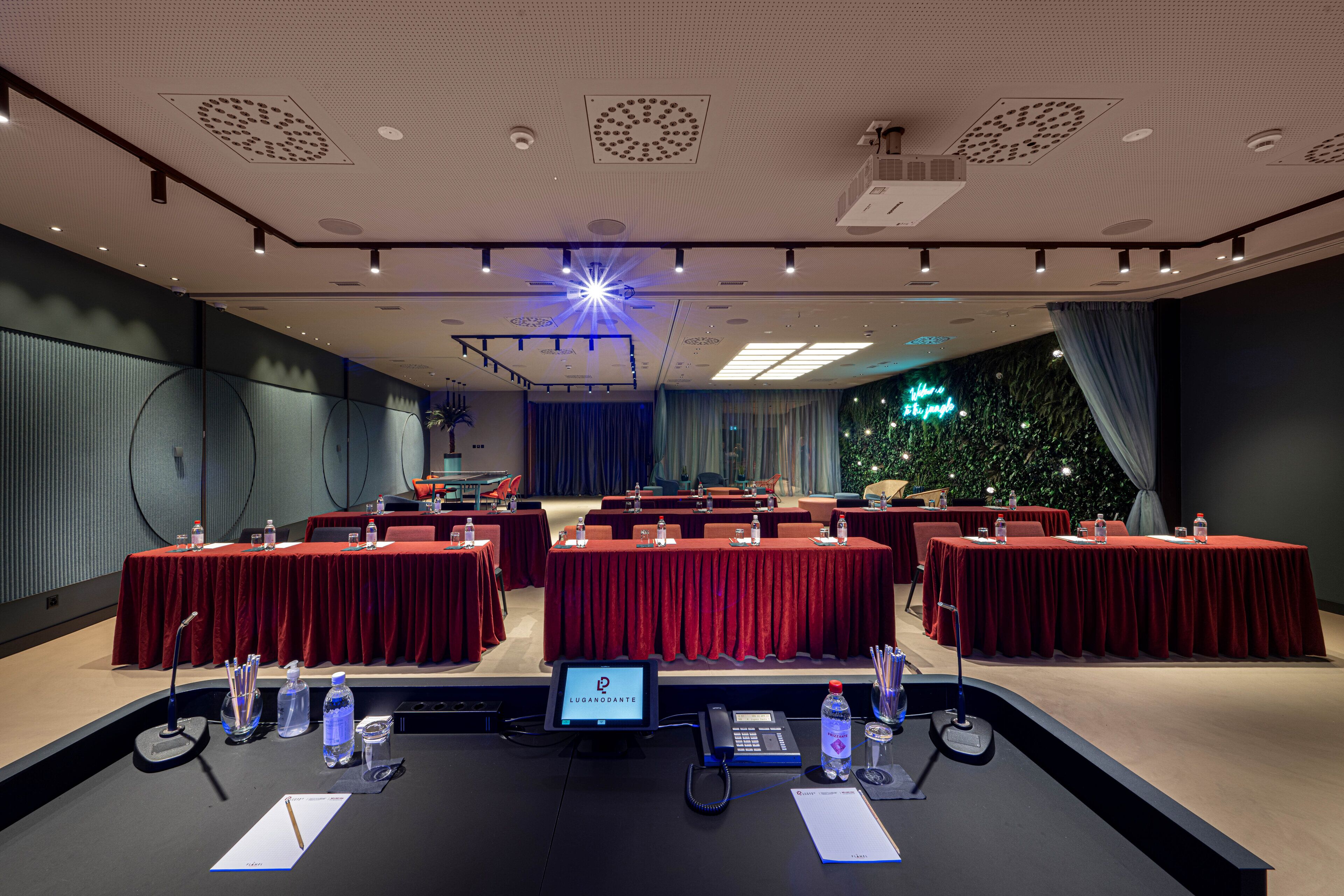 A conference room with red tables, a podium, and a digital screen.
