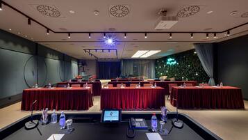 A conference room with red tables, a podium, and a digital screen.