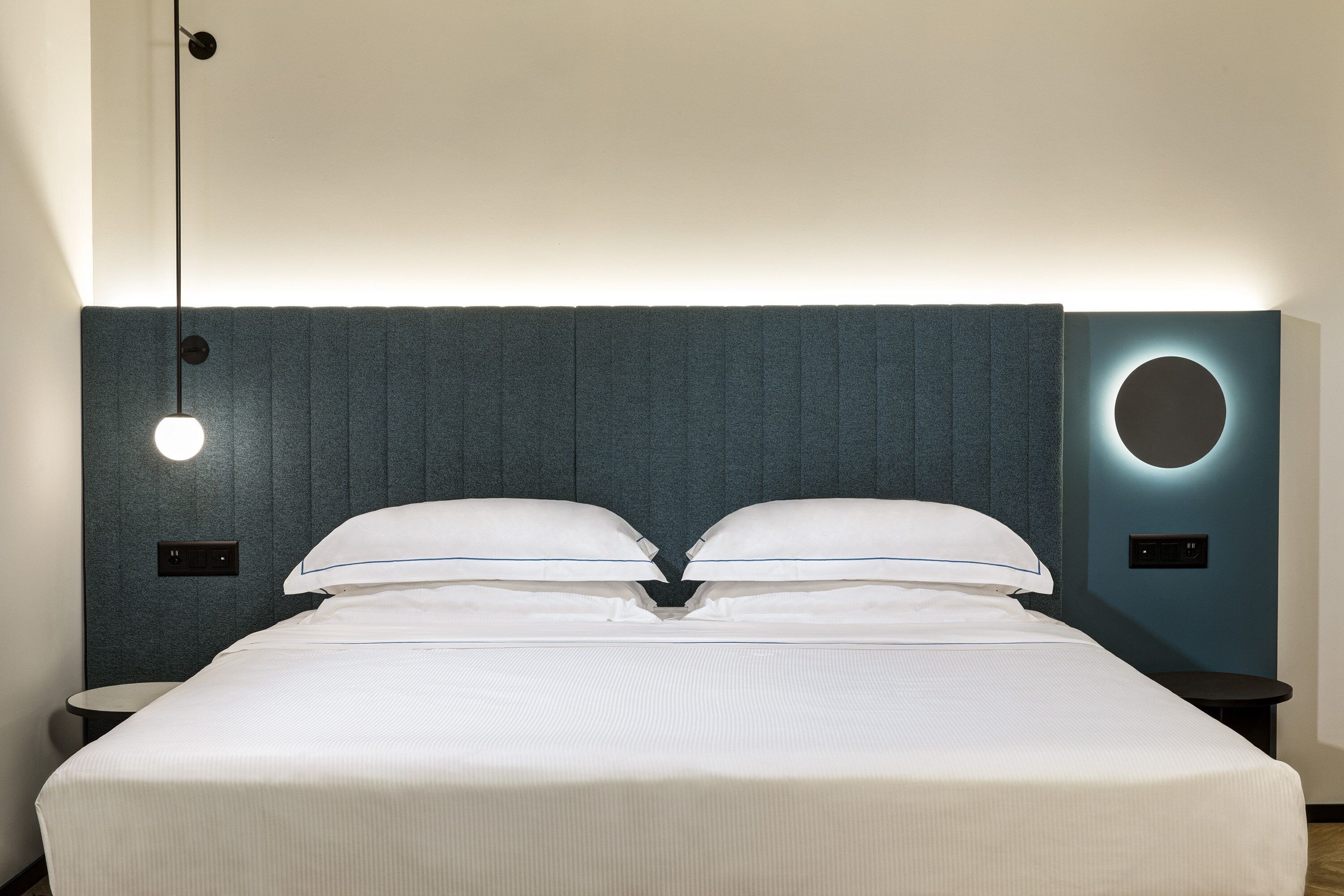 A neatly made bed with a headboard featuring a circular light fixture and a textured wall.