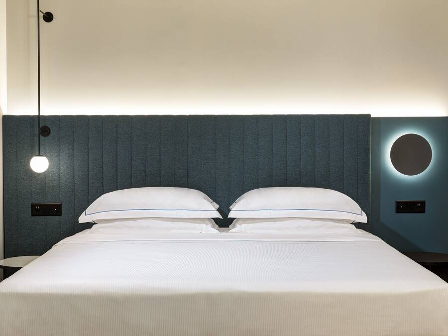 A neatly made bed with a headboard featuring a circular light fixture and a textured wall.