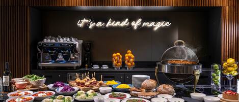 Un bufé con diversos platos, una máquina de café y un letrero de neón que dice "it's a kind of magic".