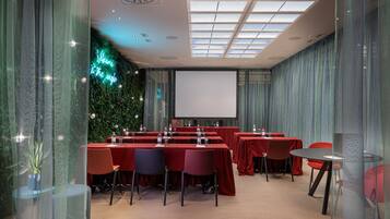 Een vergaderruimte met tafels en stoelen, een projectiescherm en een groene wand met een neonbord.