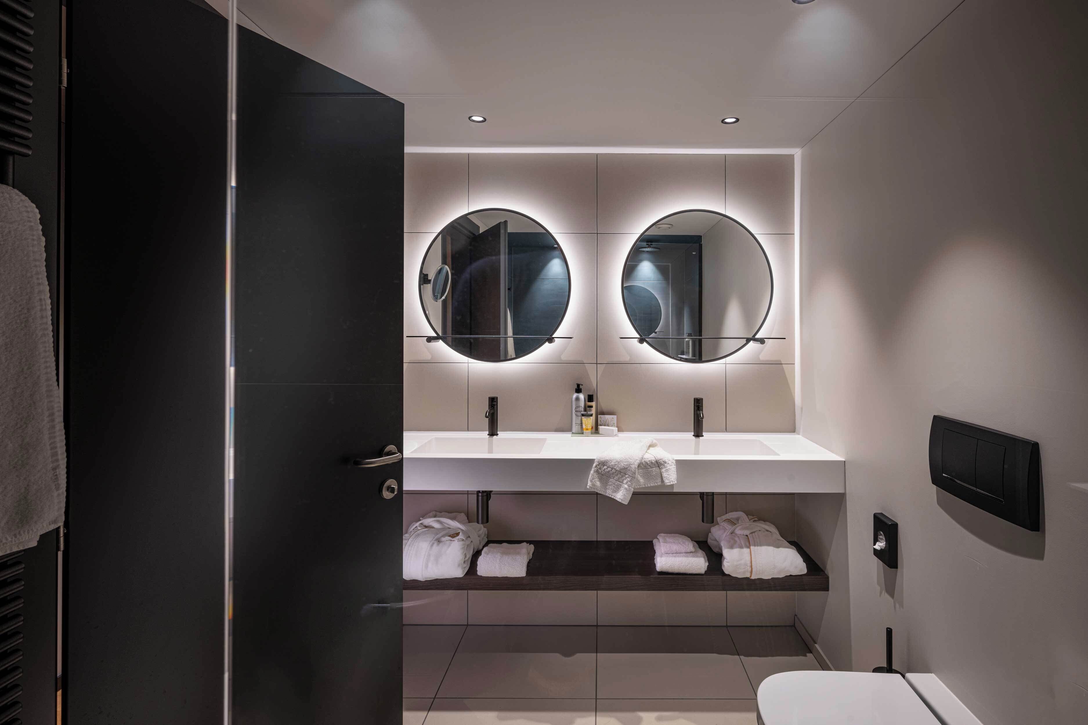 A modern bathroom with a double sink, two round mirrors, and a towel rack.