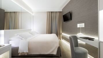 Una habitación de hotel moderna con una cama grande, un escritorio con lámpara, un televisor montado en la pared y una silla.