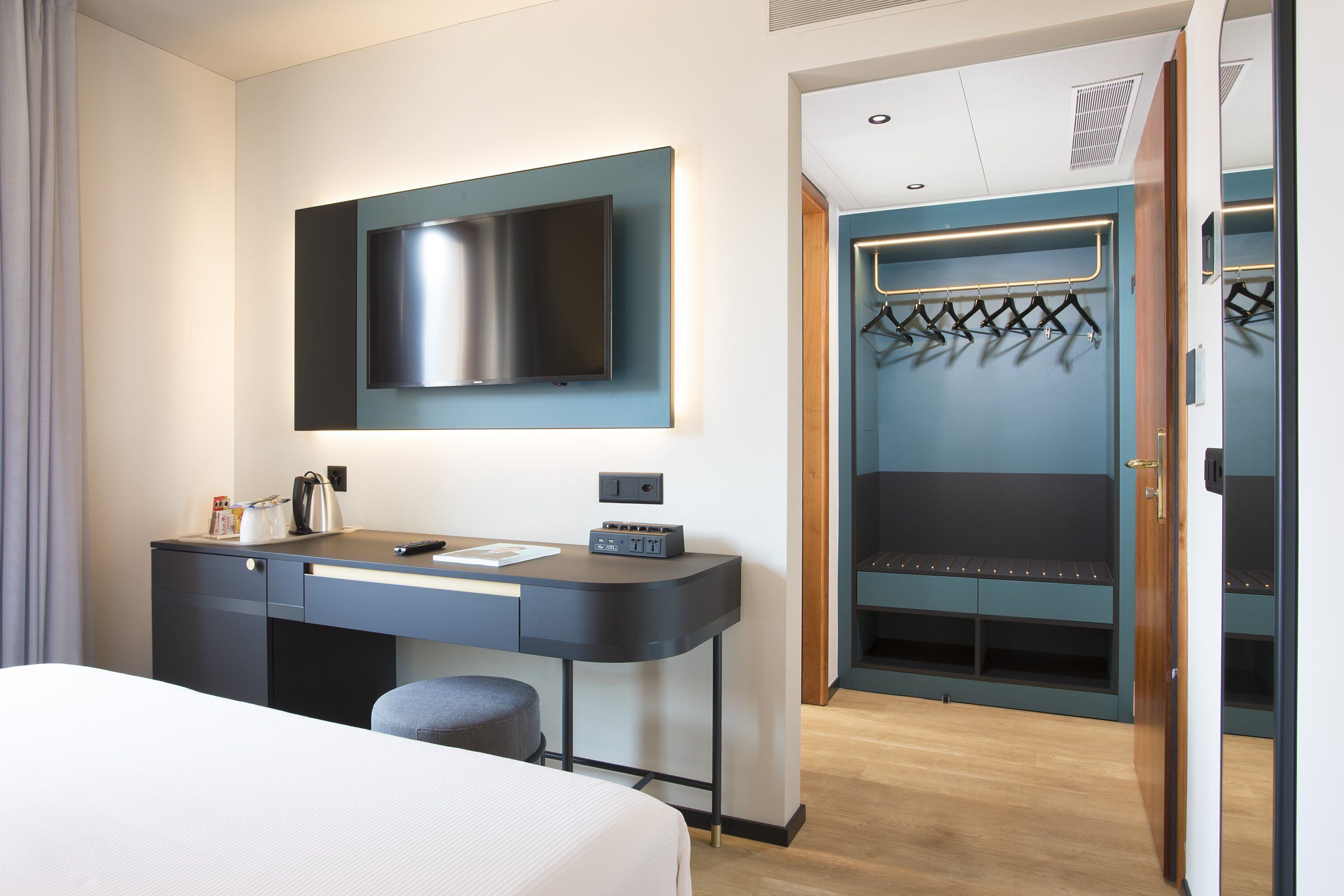 Una habitación de hotel con cama, escritorio con televisor de pantalla plana, perchero y armario.