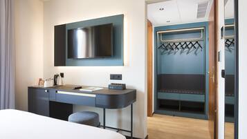 Quarto de hotel com cama, escrivaninha com televisão de tela plana, cabideiro e guarda-roupa.