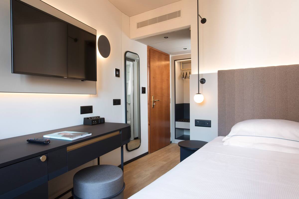 A modern hotel room with a large bed, a desk with a computer, a TV, and a mirror.