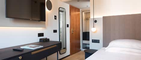 A modern hotel room with a large bed, a desk with a computer, a TV, and a mirror.