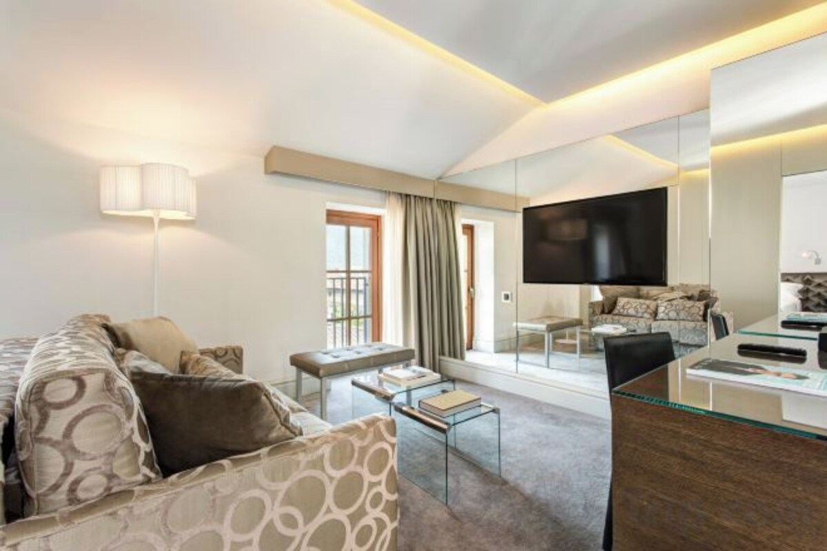 A modern hotel room with a sofa, a coffee table, a TV, and a glass partition.