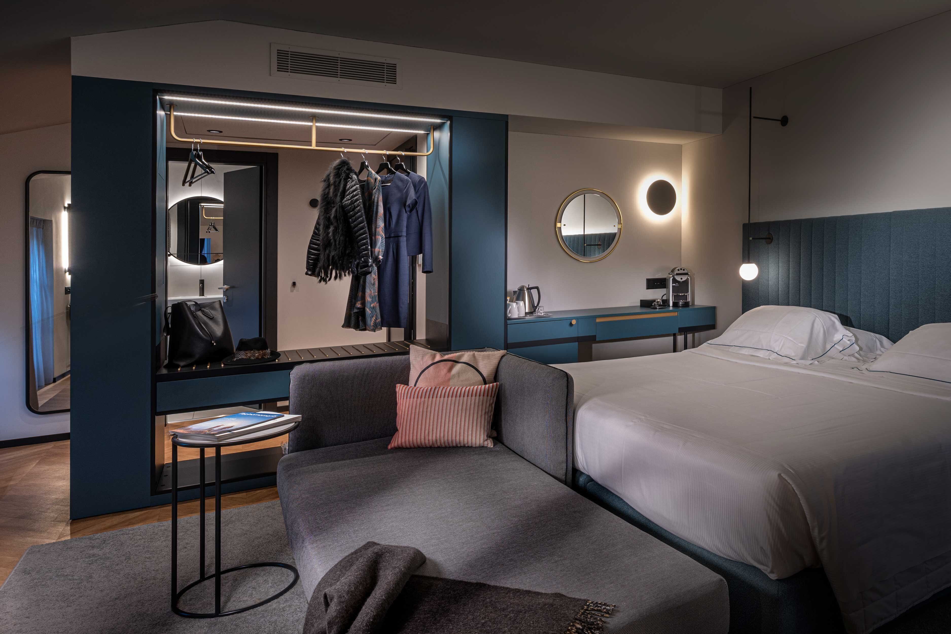 Una habitación de hotel moderna con una cama grande, un área de descanso, un tocador con espejo y un perchero.