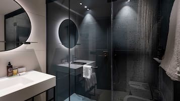 Ett modernt badrum med en dusch som är avskärmad med glasväggar, en rund spegel och en vit tvättställ.