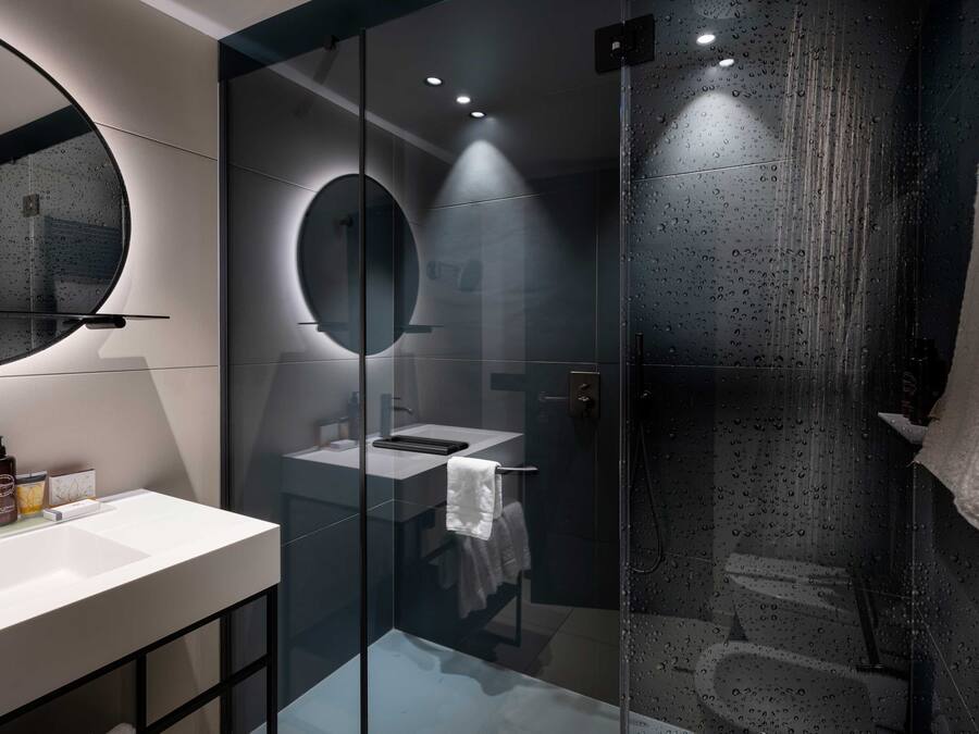 A modern bathroom with a glass-enclosed shower, a round mirror, and a white sink.