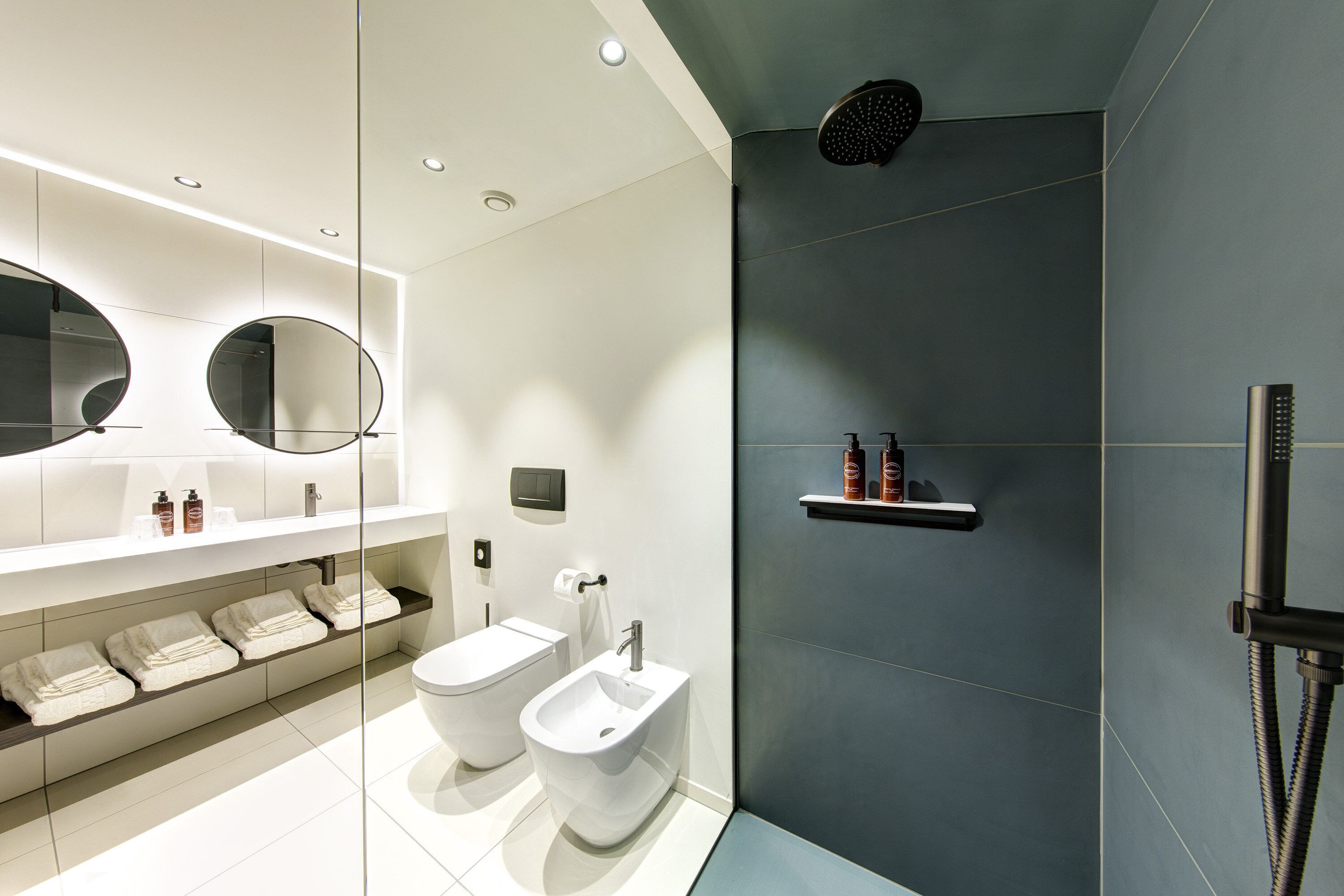 Ein modernes Badezimmer mit integriertem Bidet, Toilette, großem Spiegel und Duschbereich.