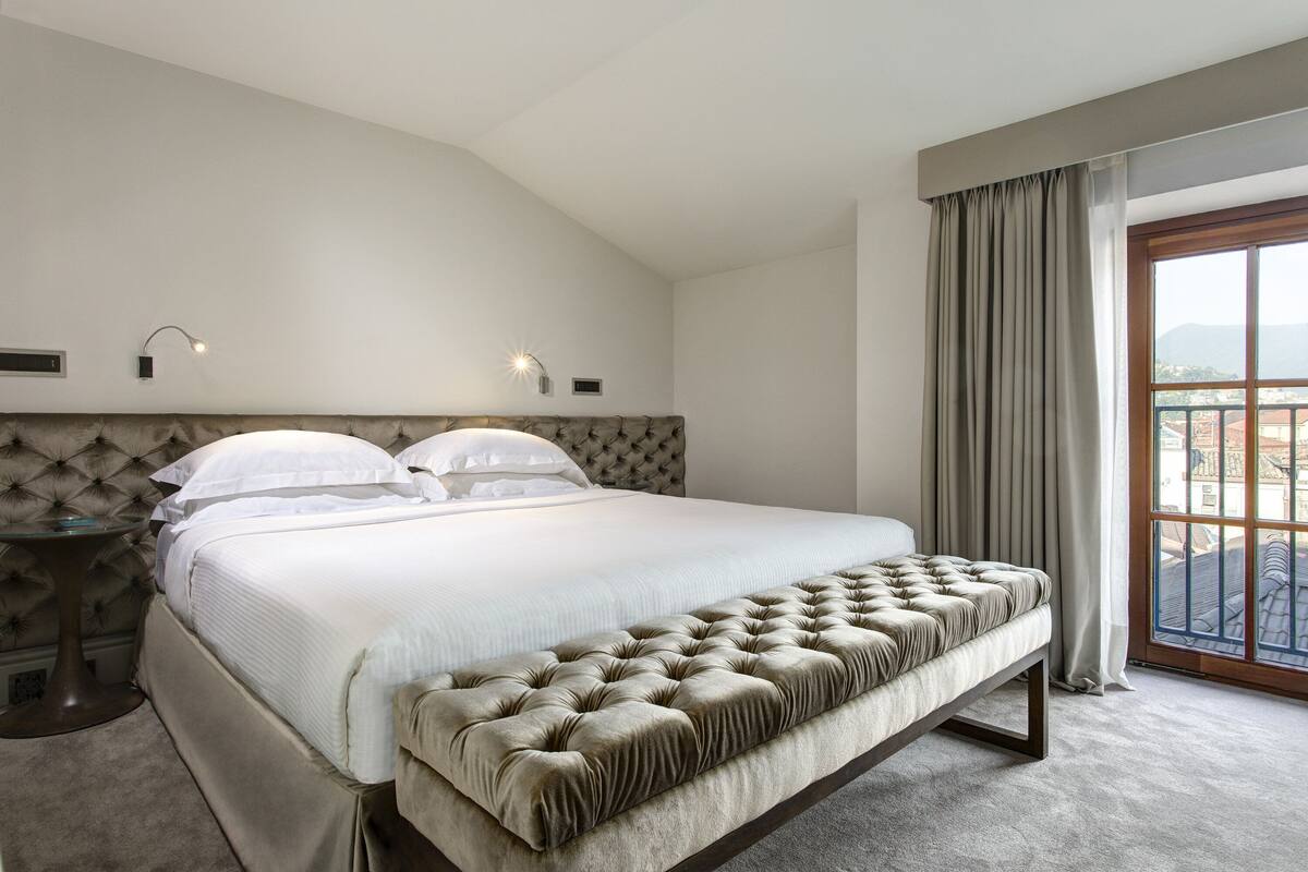 A bedroom with a large bed, a bedside table, and a window with curtains.