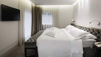 Habitación de hotel con una cama grande, un televisor de pantalla plana montado en la pared, una mesita de noche con teléfono y una ventana con cortinas traslúcidas.