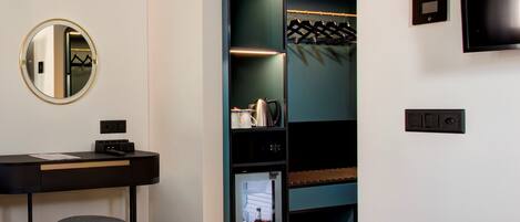 A modern hotel room with a bed, a desk with a chair, a minibar, a coat rack, and a TV mounted on the wall.