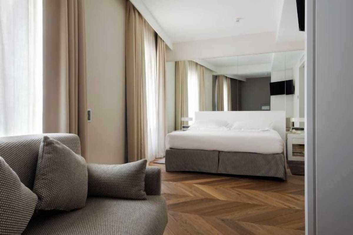A modern hotel room with a large bed, a sofa, and a wooden floor.