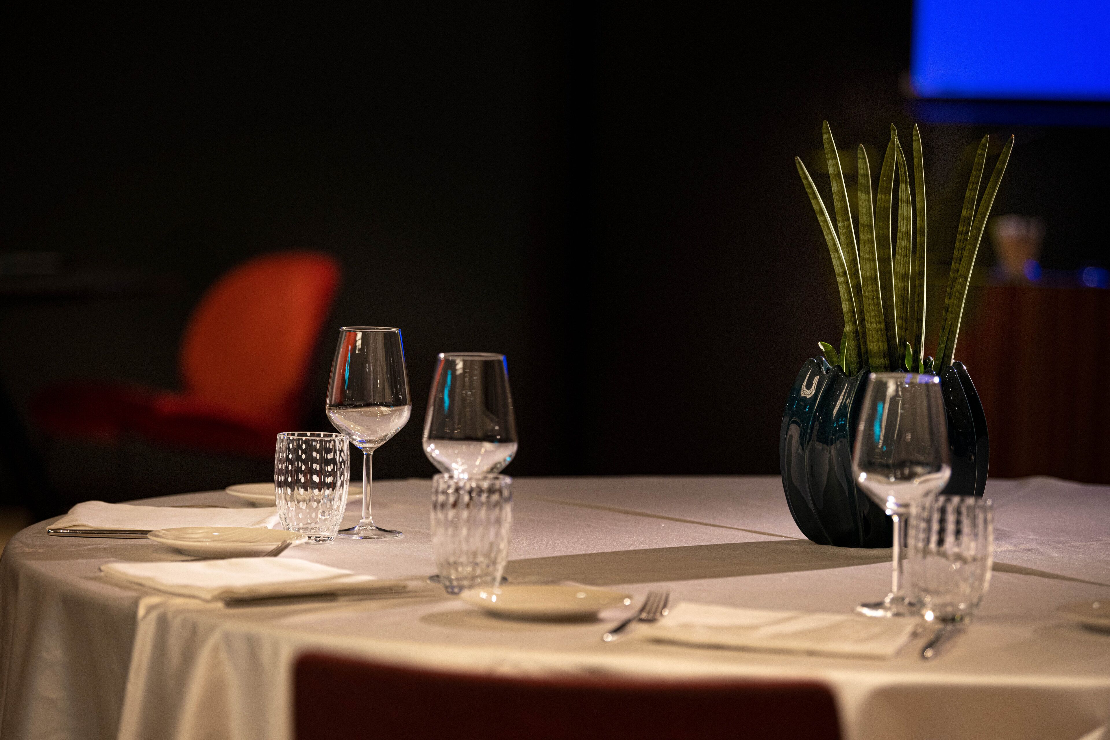 A table set for dining with clear glassware and a decorative vase with green plants.