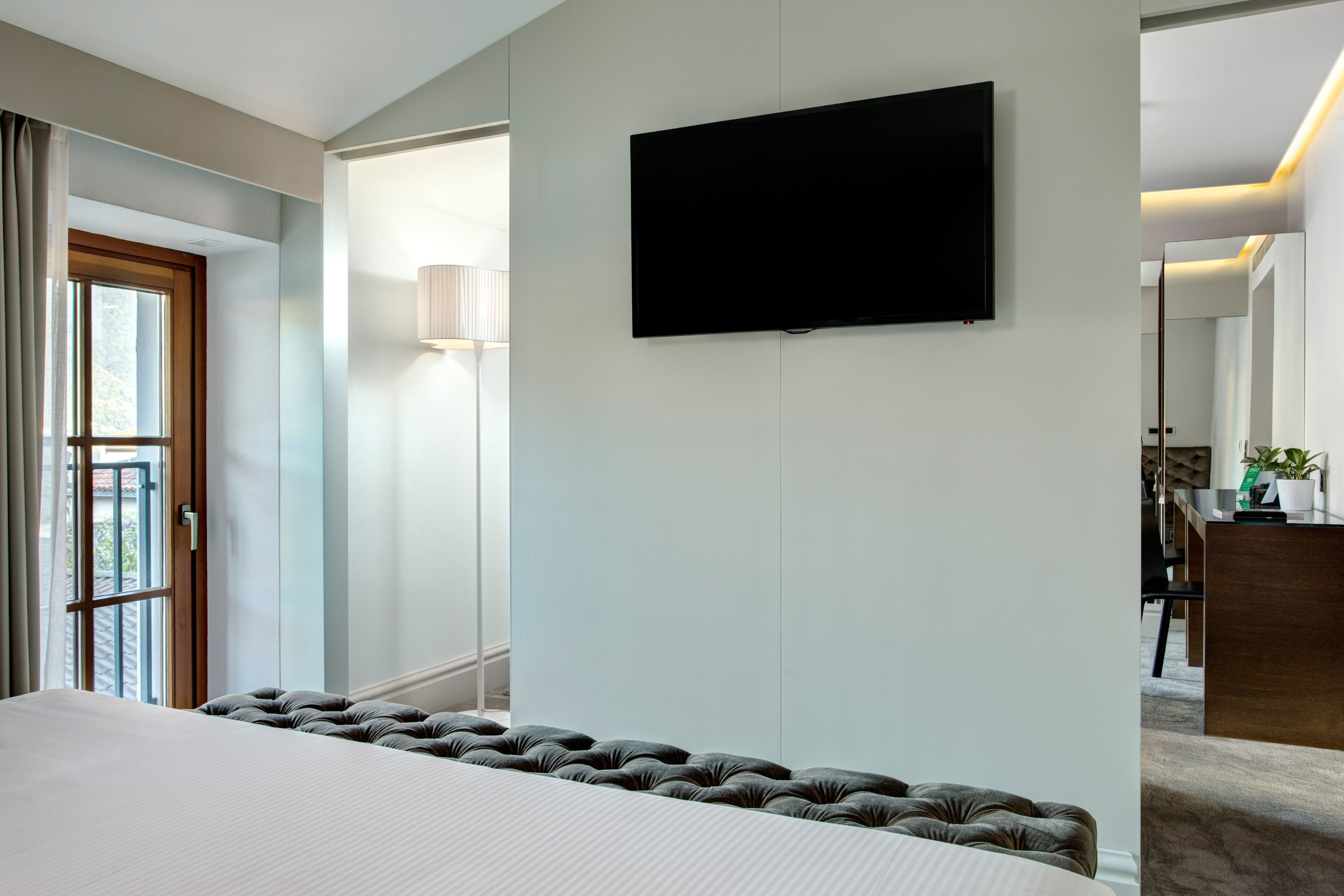 Een hotelkamer met een groot bed, een flatscreen televisie aan de muur, een bedlampje en uitzicht op de omgeving door een raam.