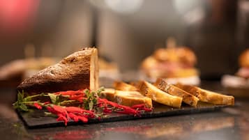 Una rebanada de pan tostado sobre una tabla de pizarra oscura con flores rojas y un pan entero al fondo.