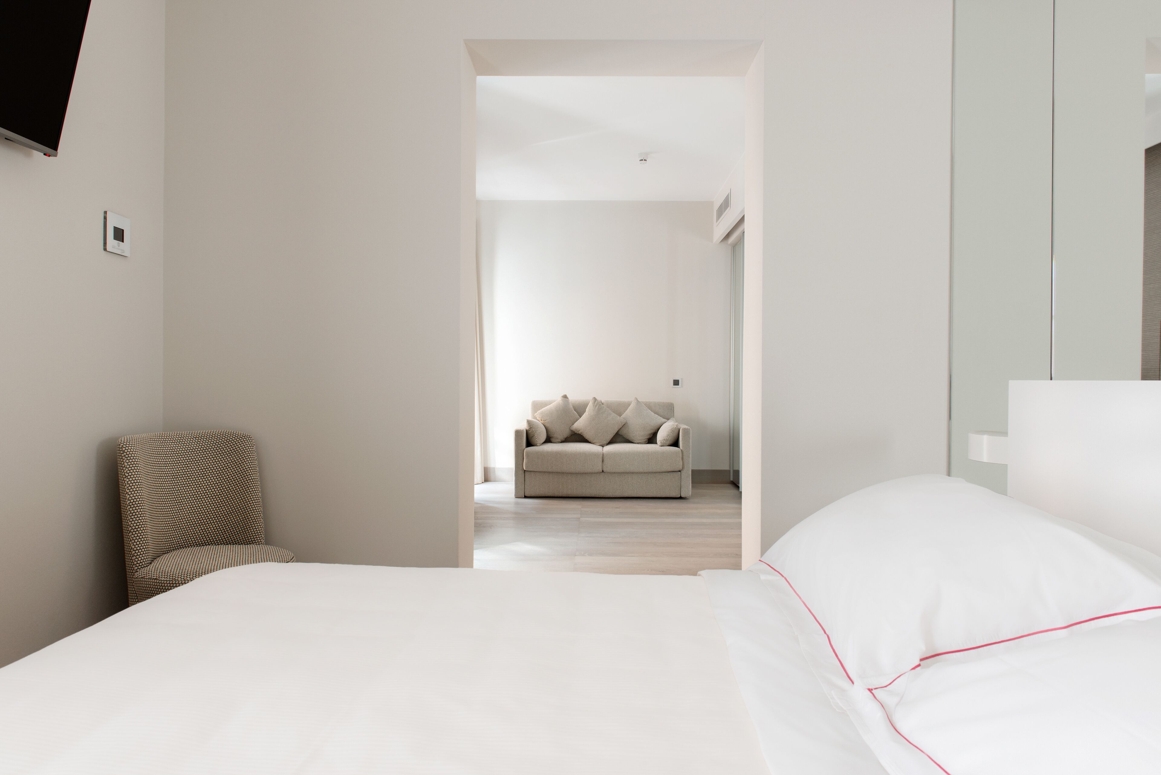 A modern bedroom with a large bed, a chair, and a sofa in the background.