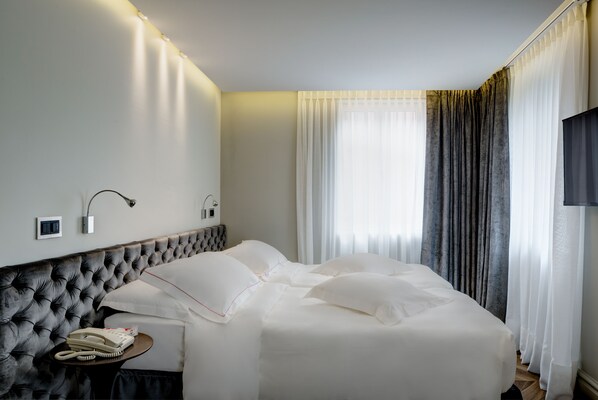 A hotel room with a tufted headboard, a bedside telephone, and a large bed with white linens. - LUGANODANTE Boutique & Lifestyle Hotel (Lugano)