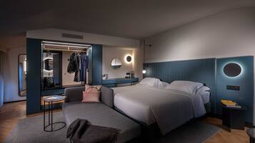 Ein modernes Hotelzimmer mit einem großen Bett, einer Sitzecke, einem Schminktisch mit Spiegel und einem Kleiderständer.