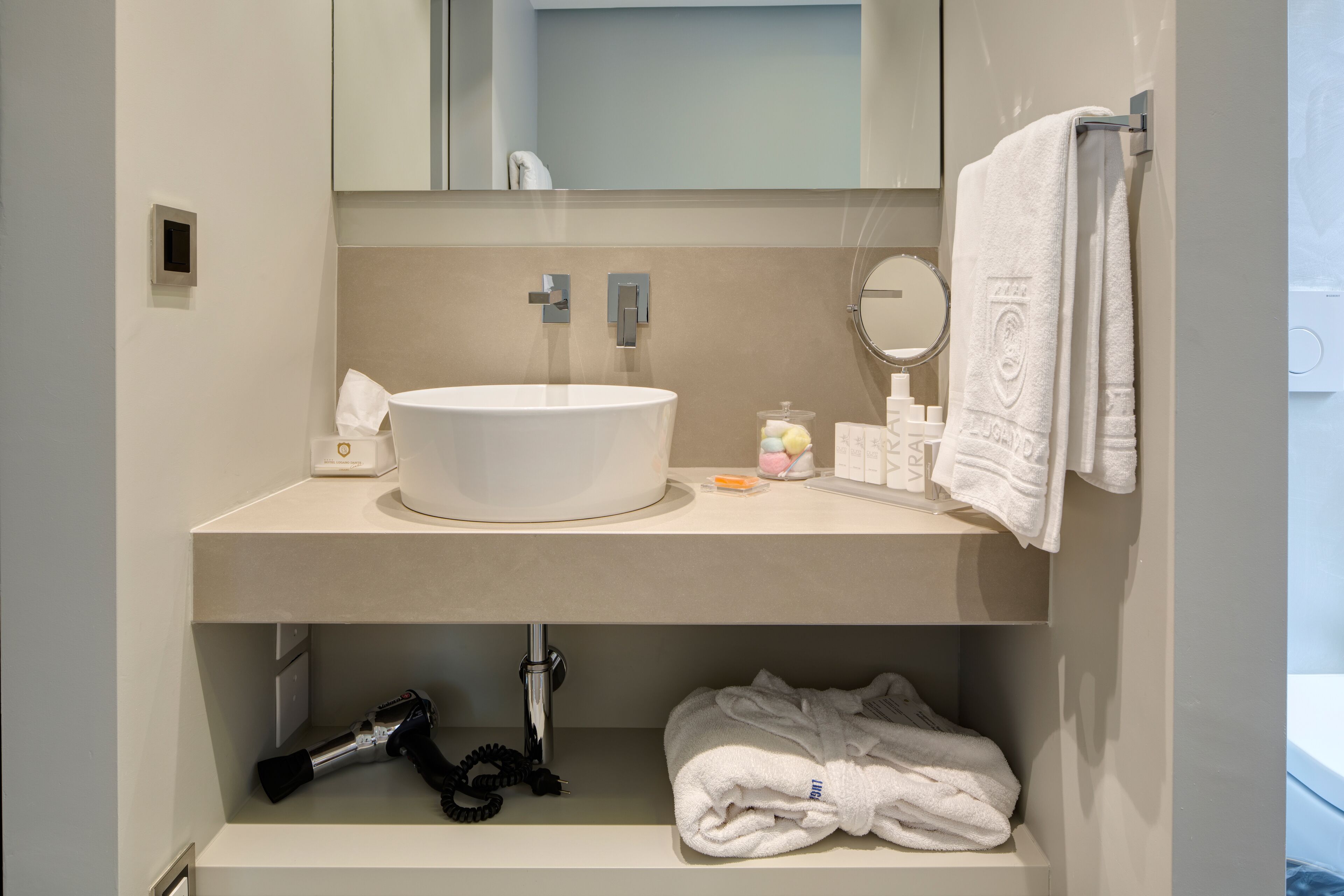 Et moderne badeværelse med en rund vask, et håndklædestativ og en hylde med toiletartikler.