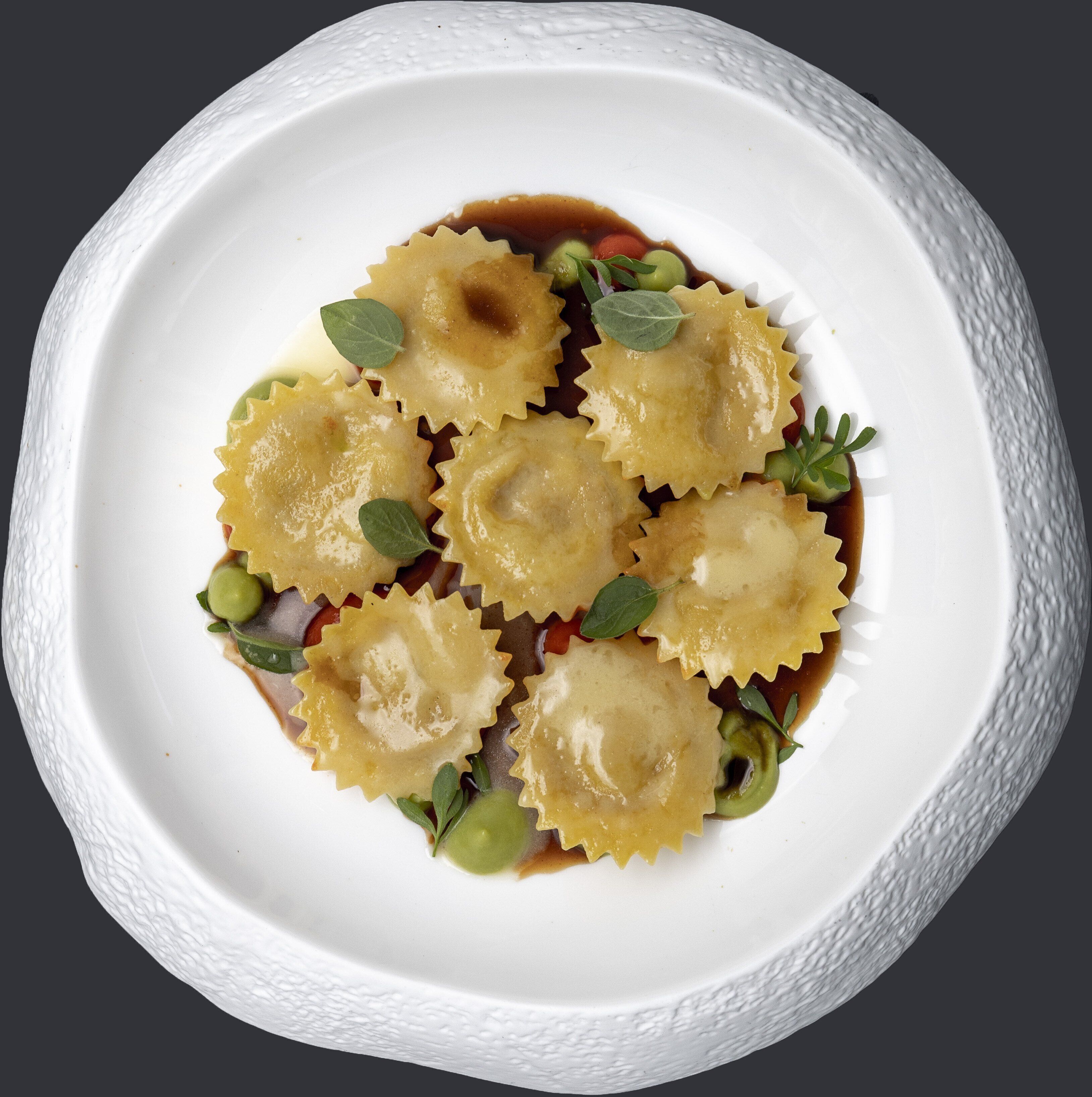 A white plate with ravioli and a brown sauce, garnished with green leaves.