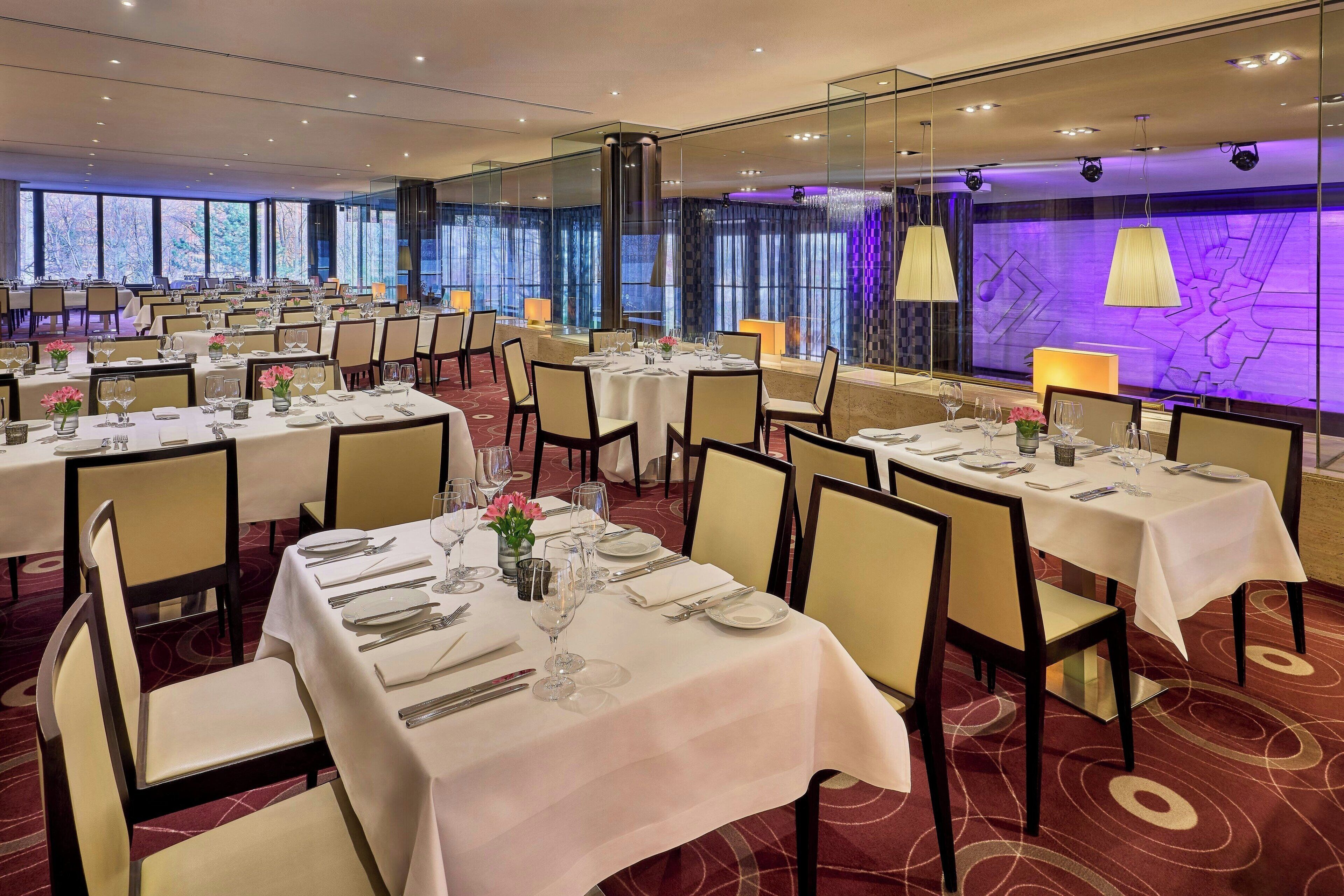 A banquet hall with multiple tables set for dining, large windows, and a modern interior design.