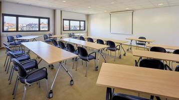 A classroom with rows of desks and chairs, large windows with a city view, and a projection screen on the wall.
