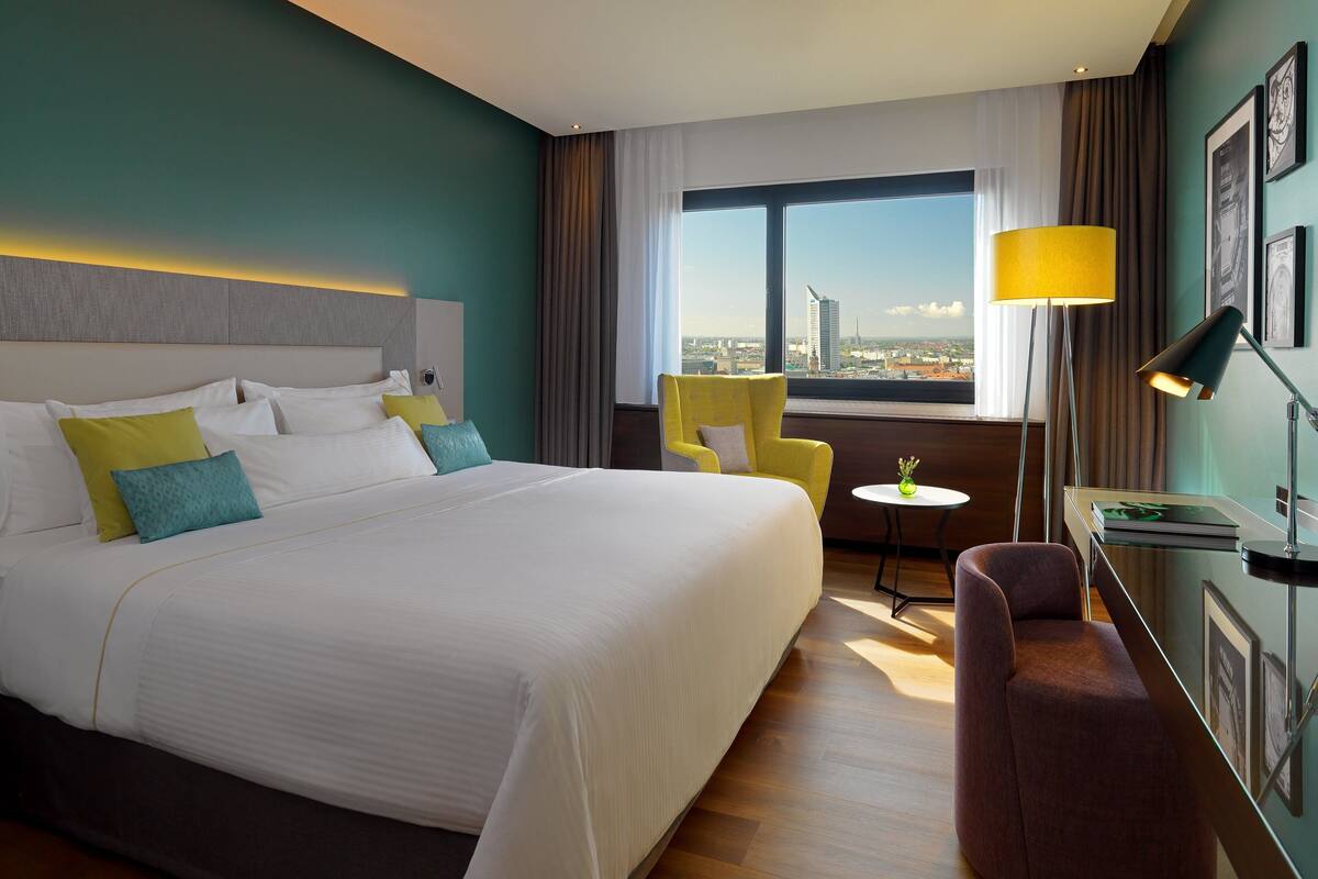 Habitación de hotel con una cama grande, un escritorio, una silla, una mesita y vistas a la ciudad.