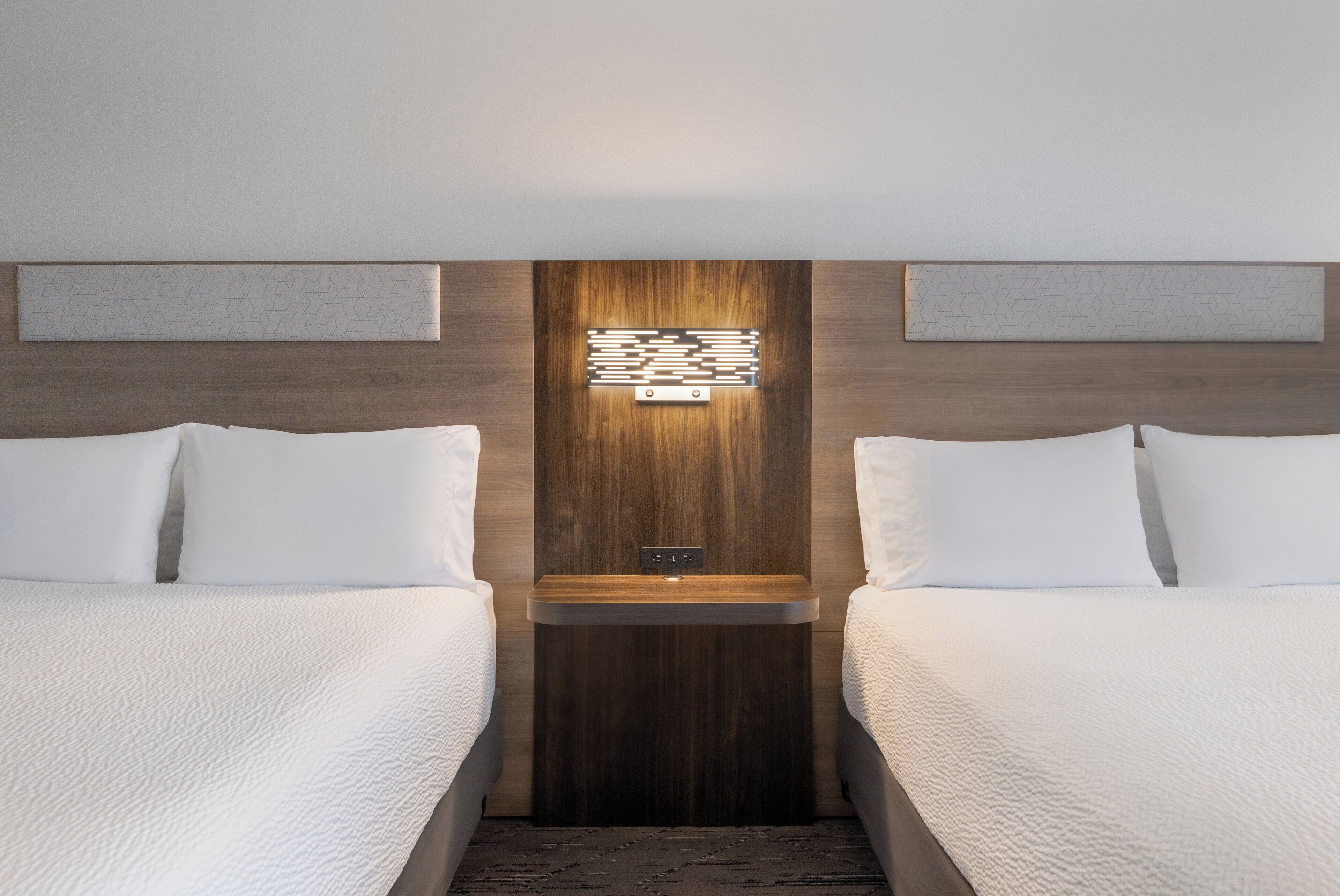 Hotellihuone, jossa on kaksi sänkyä, puinen pääty ja seinään kiinnitetty valaisin.