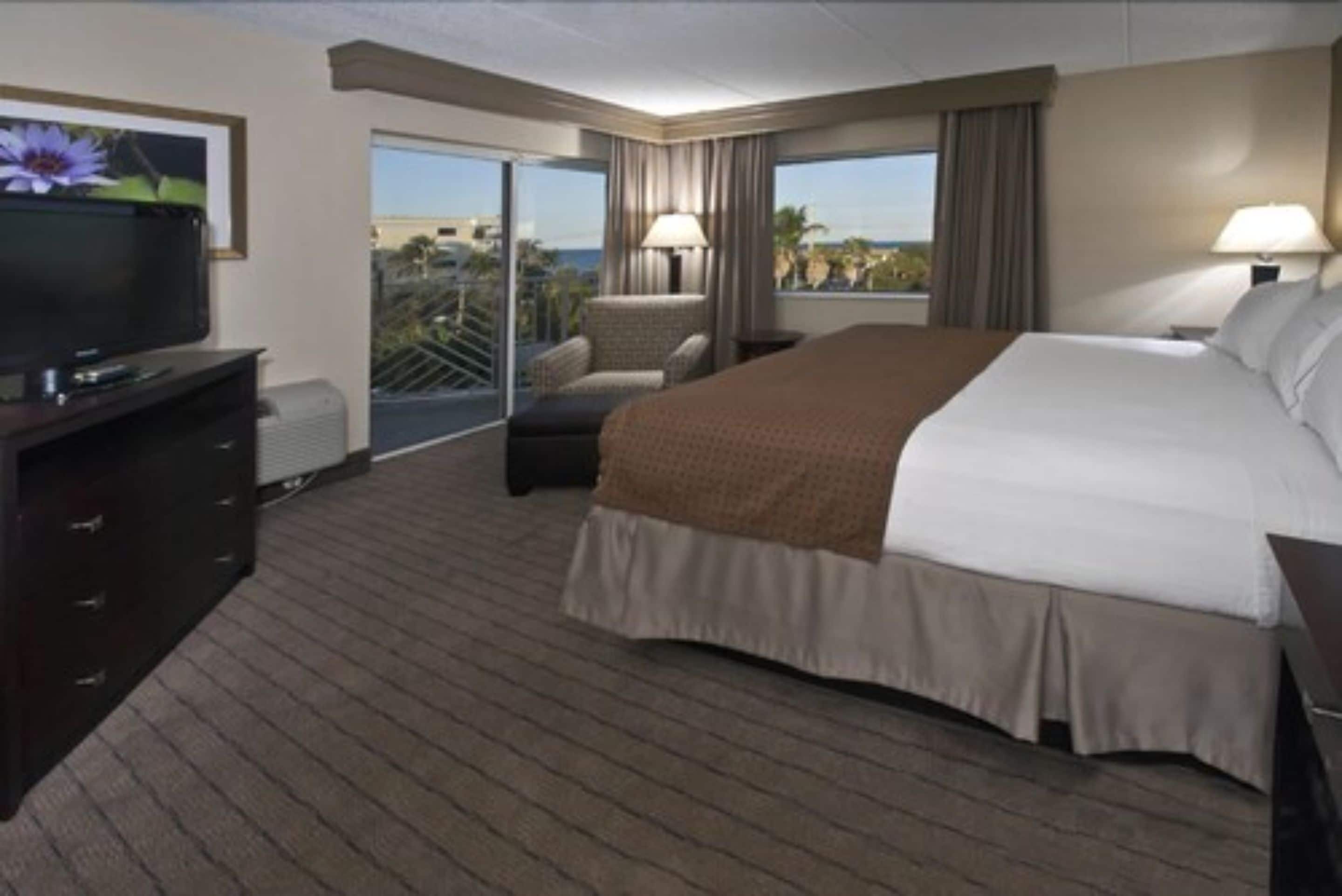 Une chambre d’hôtel avec un lit, une télévision, une chaise et une vue sur l’extérieur.