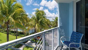 Un balcon avec une chaise bleue, une balustrade blanche et une vue sur des palmiers et une piscine.